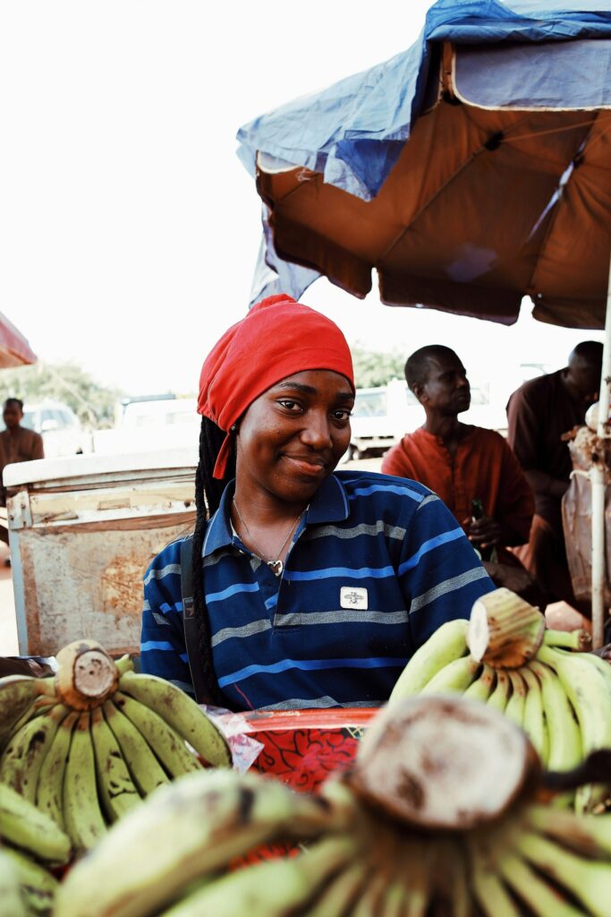A woman in a red headscarf at a market stall with bunches of bananas