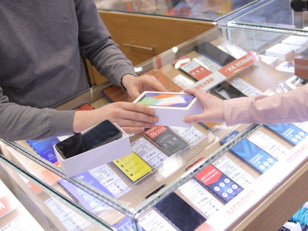 A man and a woman handing over a mobile phone at a store counter