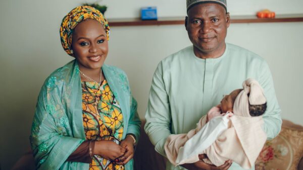 A couple in traditional Nigerian attire holding their newborn baby indoors