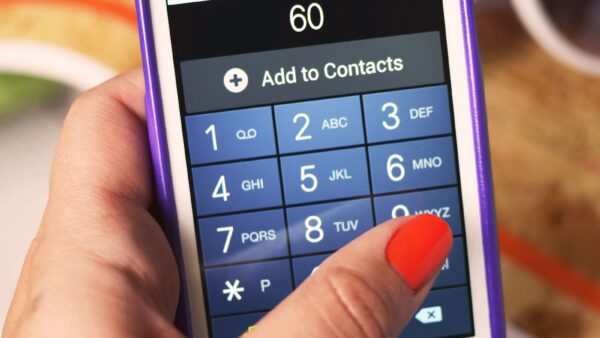 A hand with orange nail polish dialling on a smartphone number pad