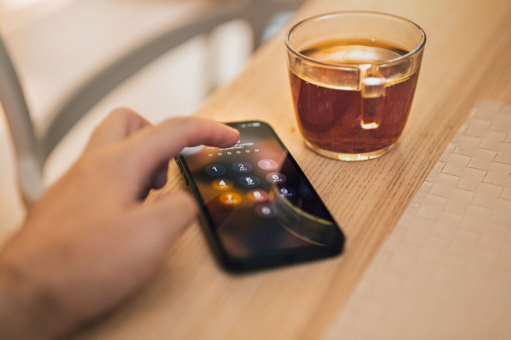 A hand unlocking a smartphone on a wooden table beside a cup of tea