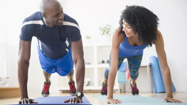 Man and woman in their 30s doing push-ups on exercise mats during a home workout.