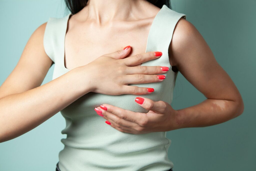 A woman in a white top doing a breast self-examination against a teal background